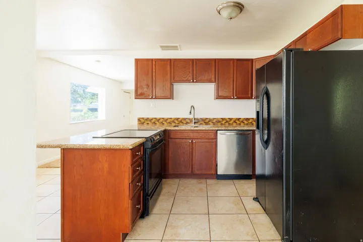Kitchen featuring tile flooring, wood-finish cabinetry, a granite-finish countertop, stainless steel dishwasher, and a black electric range