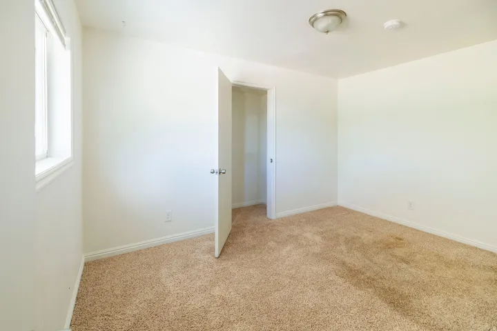 Carpeted room featuring a window with white trim, a flush-mount ceiling light fixture, a closet with a white door, and white baseboards