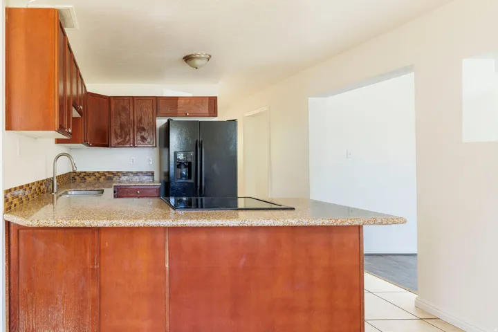 Kitchen featuring rich wood cabinetry, stone-finish countertops, a mosaic tile backsplash, and a built-in black cooktop