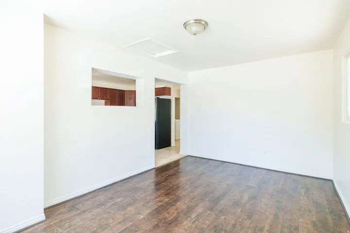 Bright living area featuring wood-finish flooring, white baseboards, and a pass-through window to the kitchen