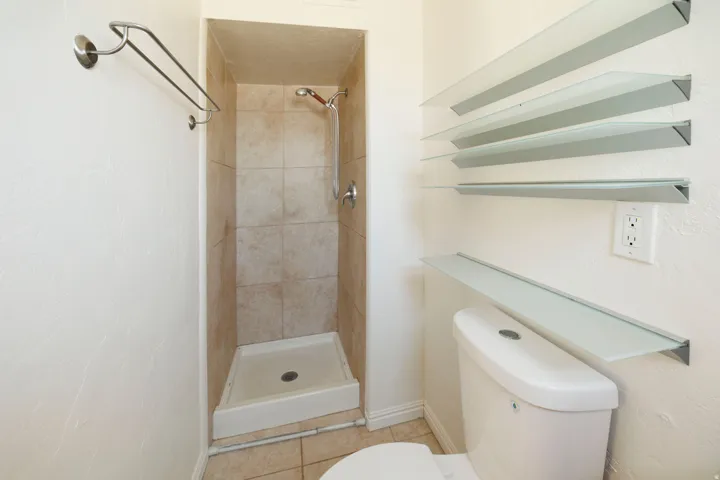 Compact shower stall with neutral tile surround, white shower pan, and chrome fixtures