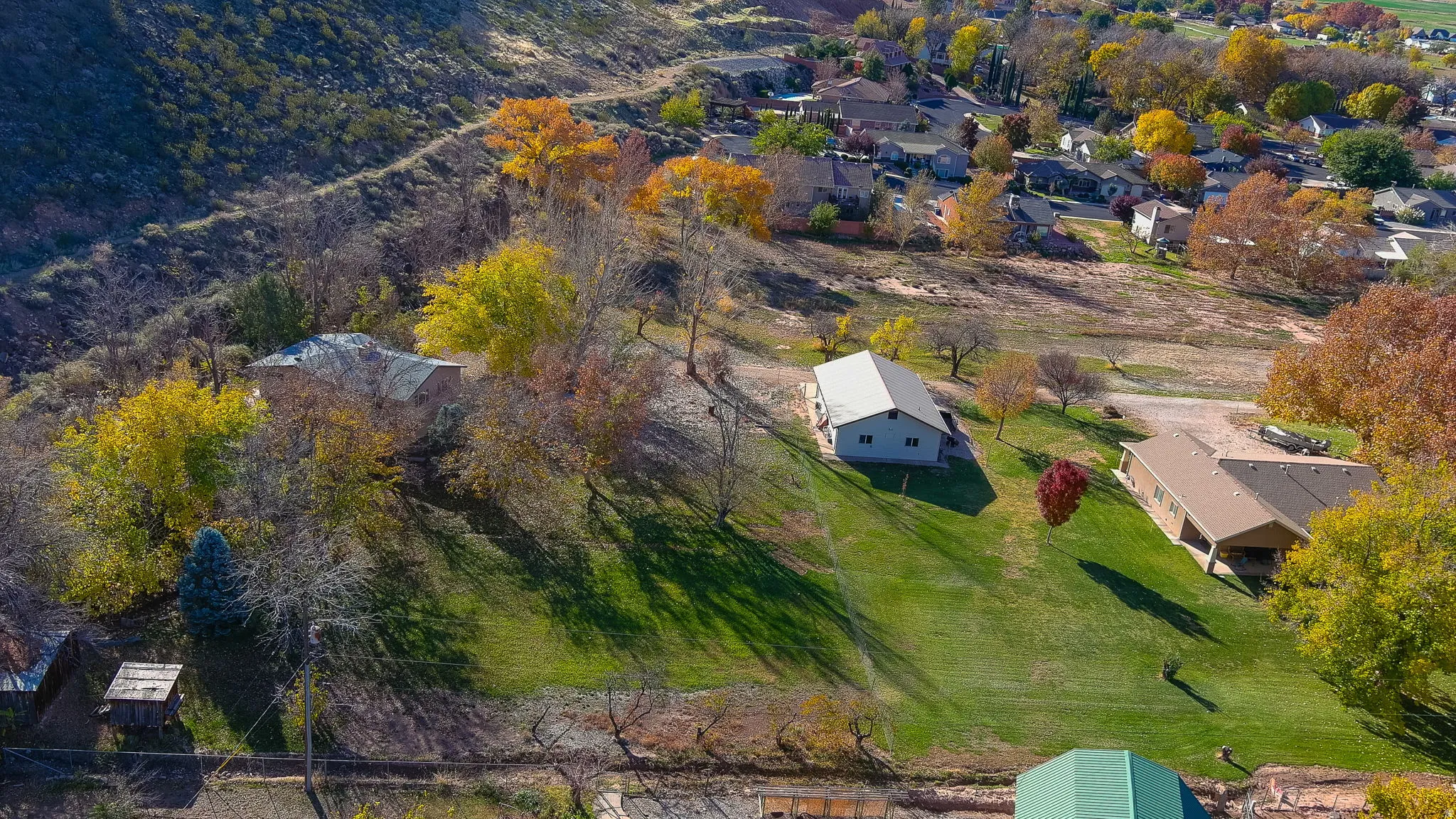 Expansive property featuring a sloping green lawn, a single-story building with a light-colored roof, and mature trees with autumn foliage