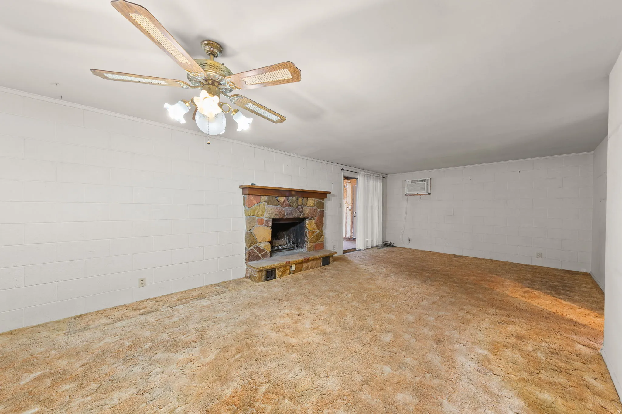 Living area featuring a stone-faced fireplace with a wood mantel, overhead ceiling fan with lighting, and a wall-mounted air conditioning unit