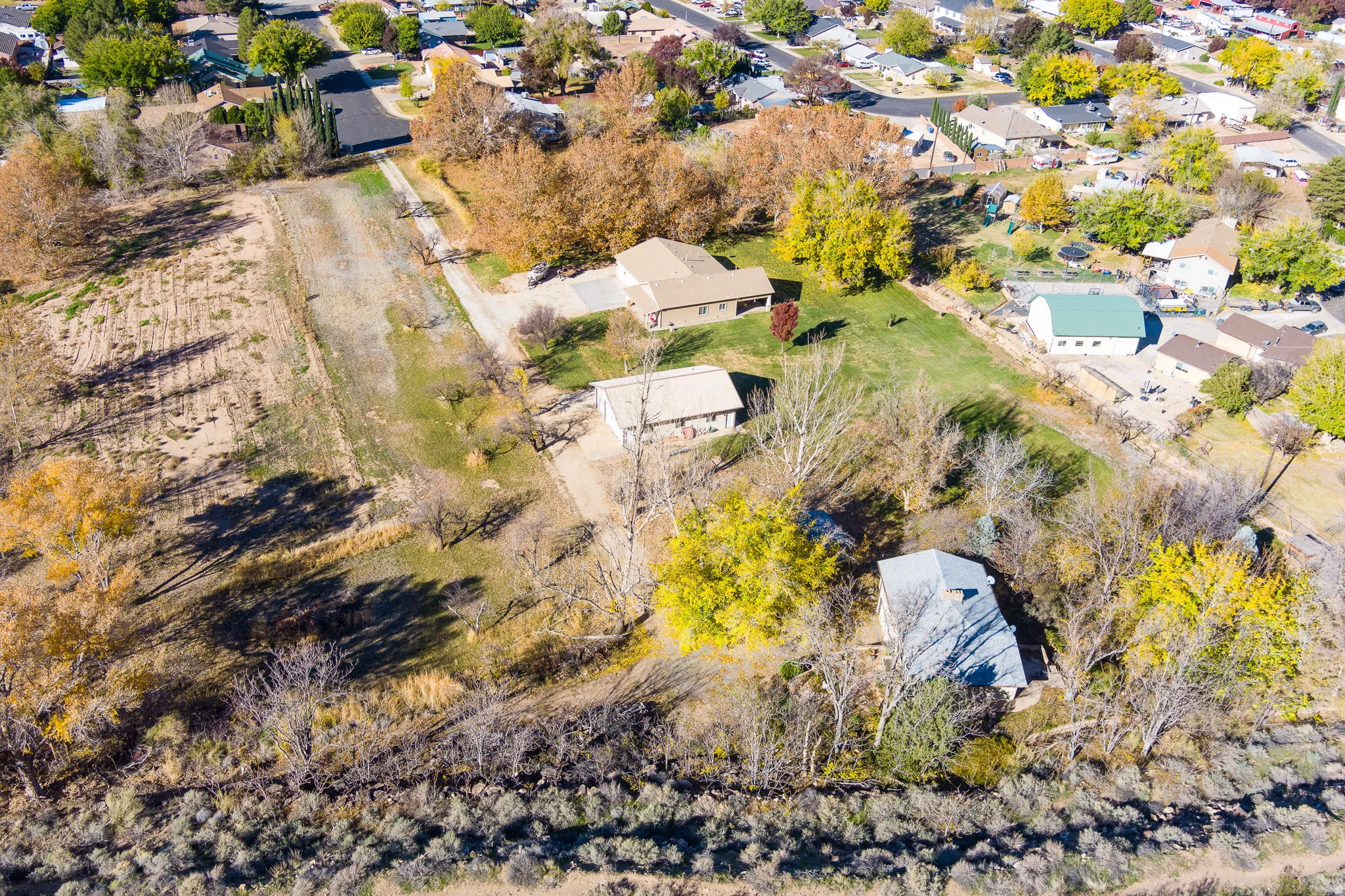 Expansive property featuring a large land parcel, established residential structures, surrounding mature trees, and nearby developed neighborhoods