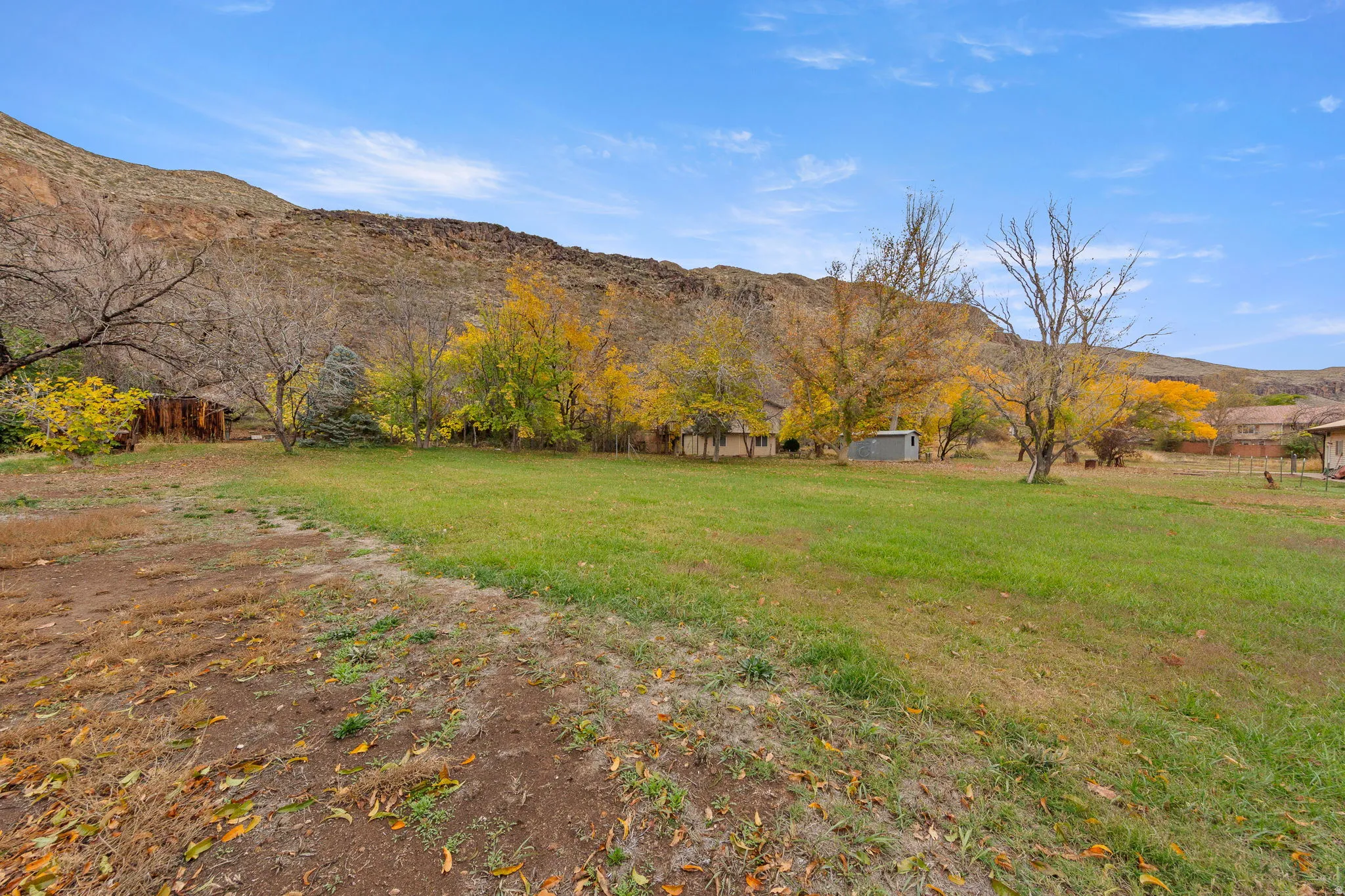 Expansive green space with distant structures and varied foliage, set against a mountainous backdrop