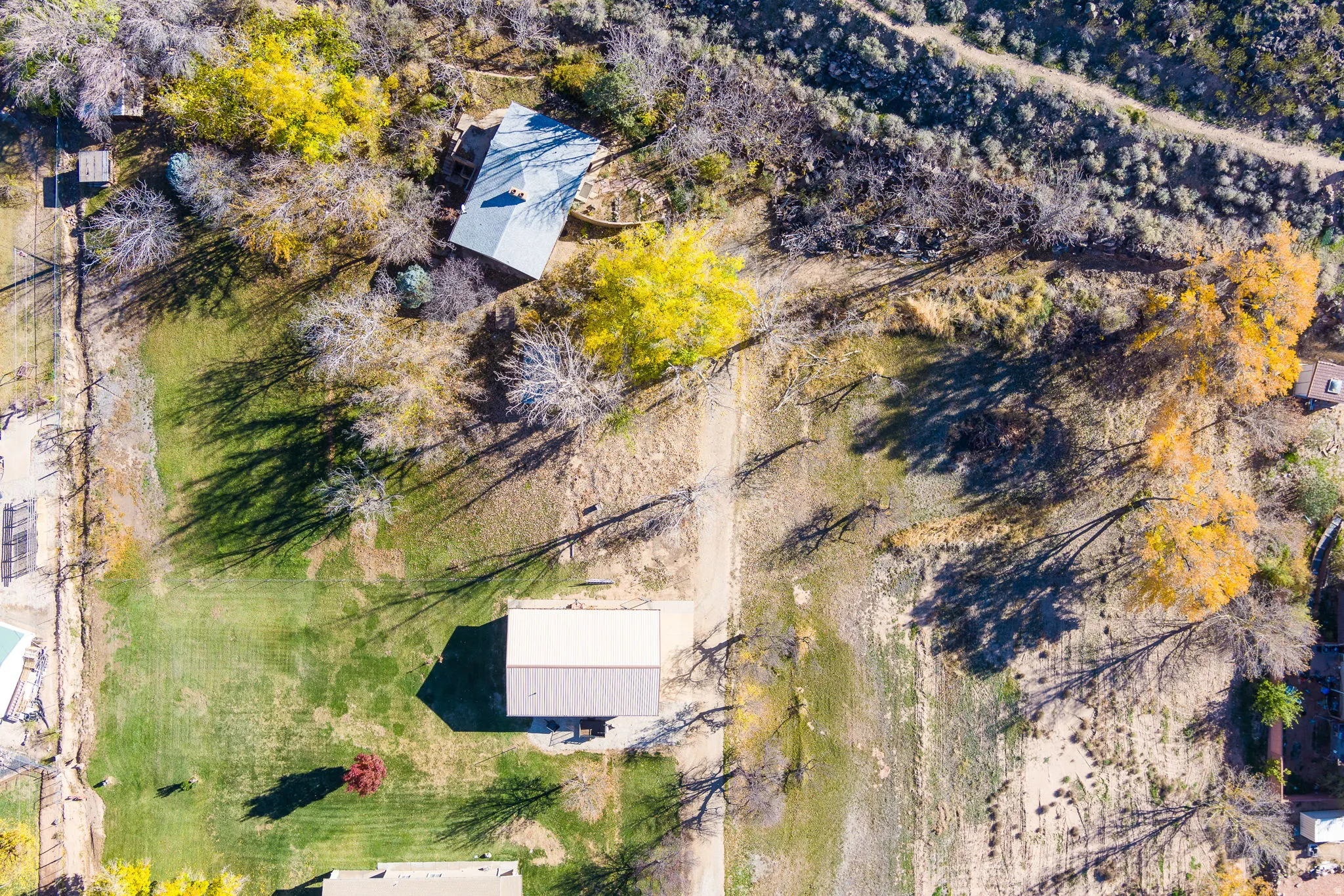 Sprawling property featuring a prominent main residence with a light-colored roof, multiple outbuildings, varied mature trees including vibrant yellow foliage, extensive natural landscaping, and distinct green lawn areas