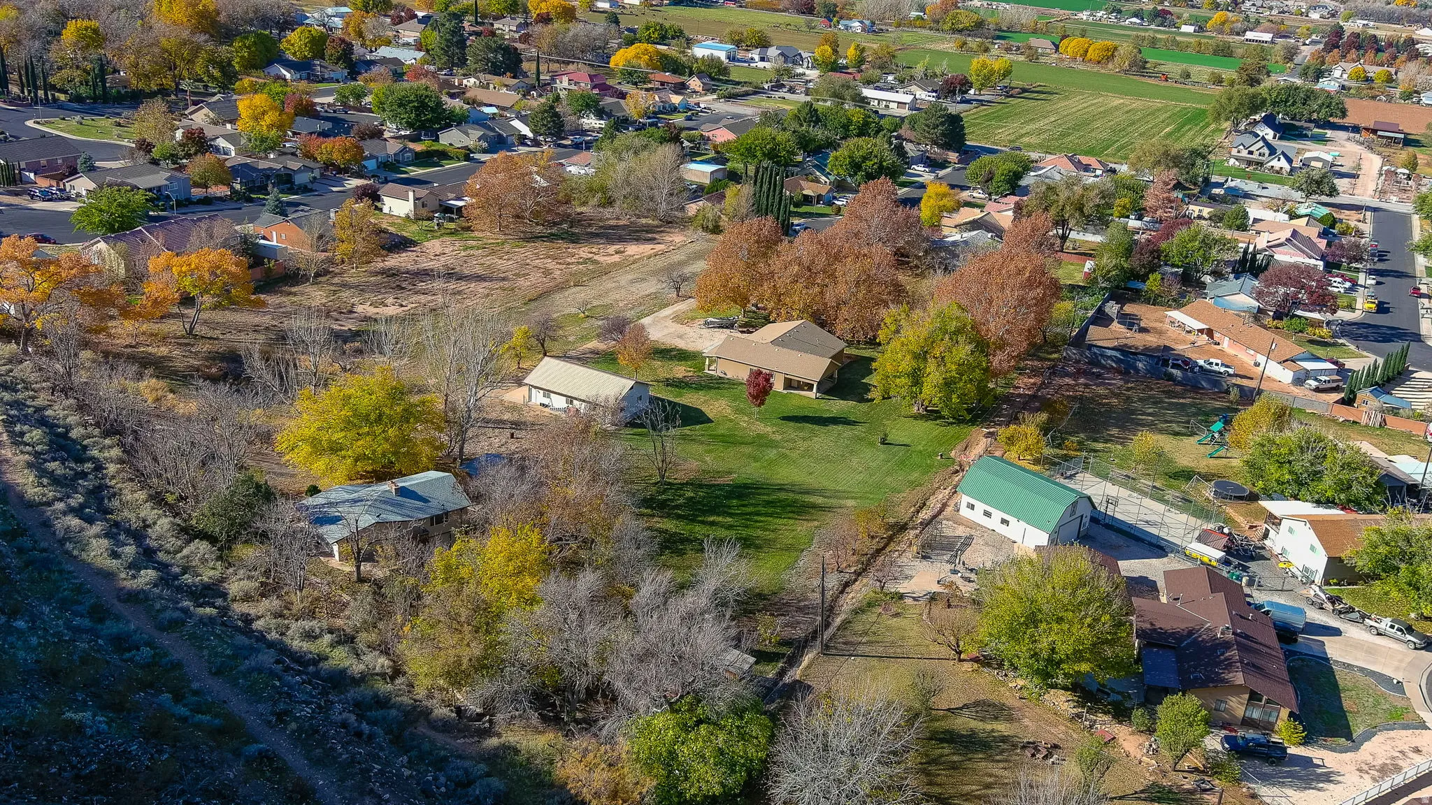 Expansive property featuring a main residence, secondary detached structure, and a large green-roofed outbuilding with an adjacent paved area