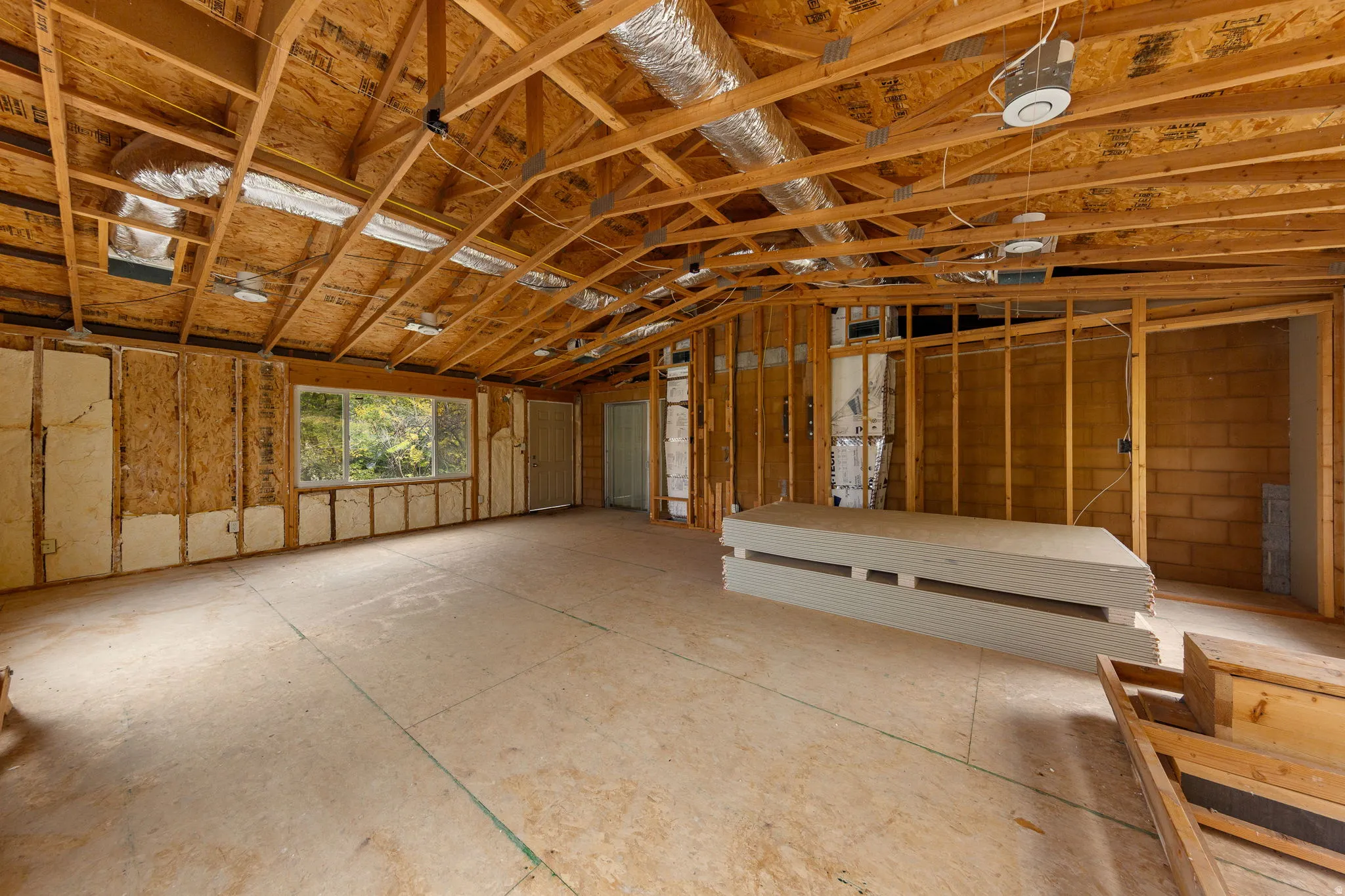 Spacious unfinished interior with exposed wooden framing and ductwork, featuring multiple windows, a concrete block wall, and a full-light exterior door