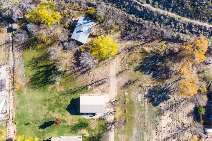 Sprawling property featuring a prominent main residence with a light-colored roof, multiple outbuildings, varied mature trees including vibrant yellow foliage, extensive natural landscaping, and distinct green lawn areas