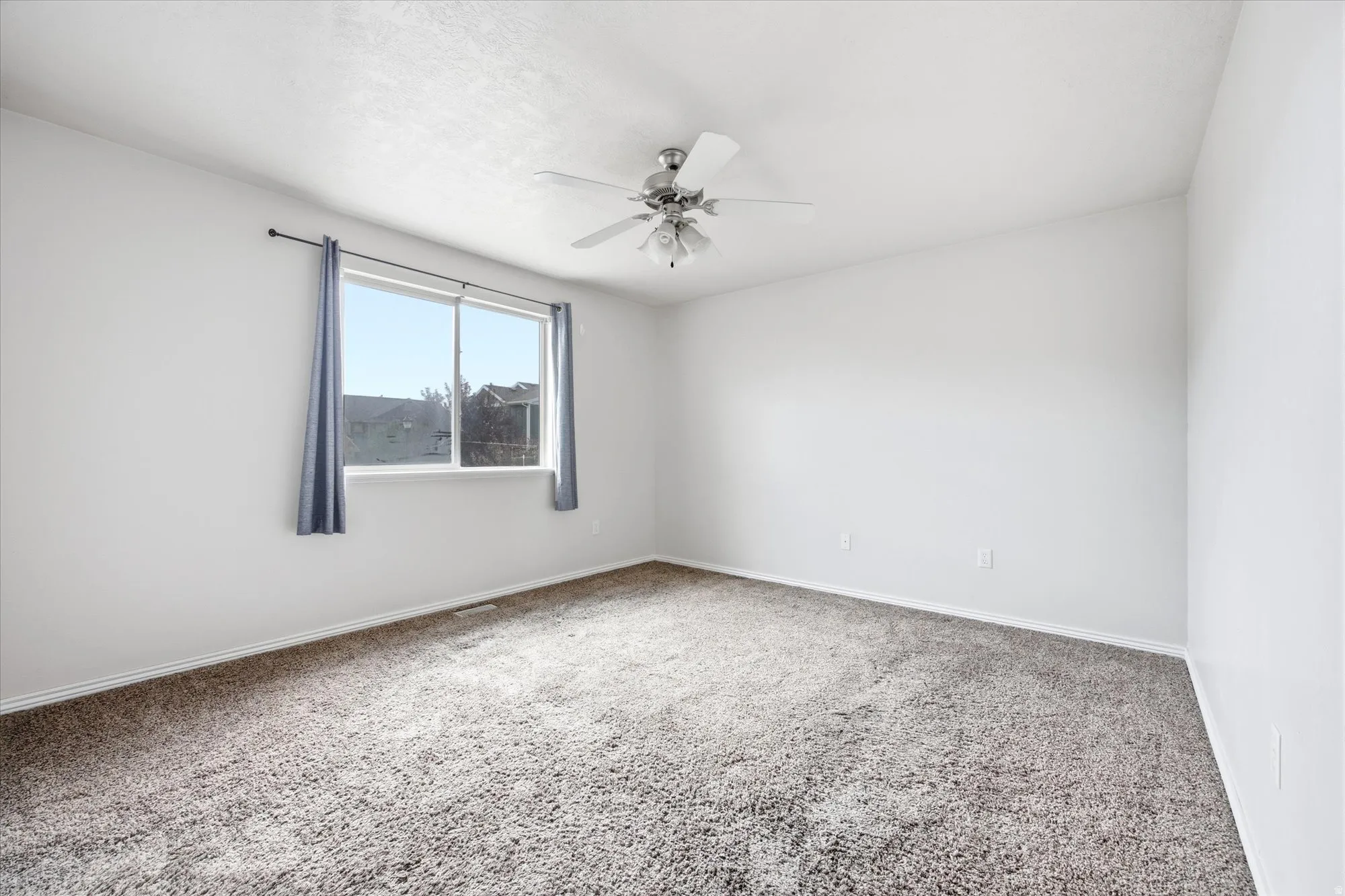 Bright room featuring a large window, neutral carpeting, white walls, and a ceiling fan with integrated lighting
