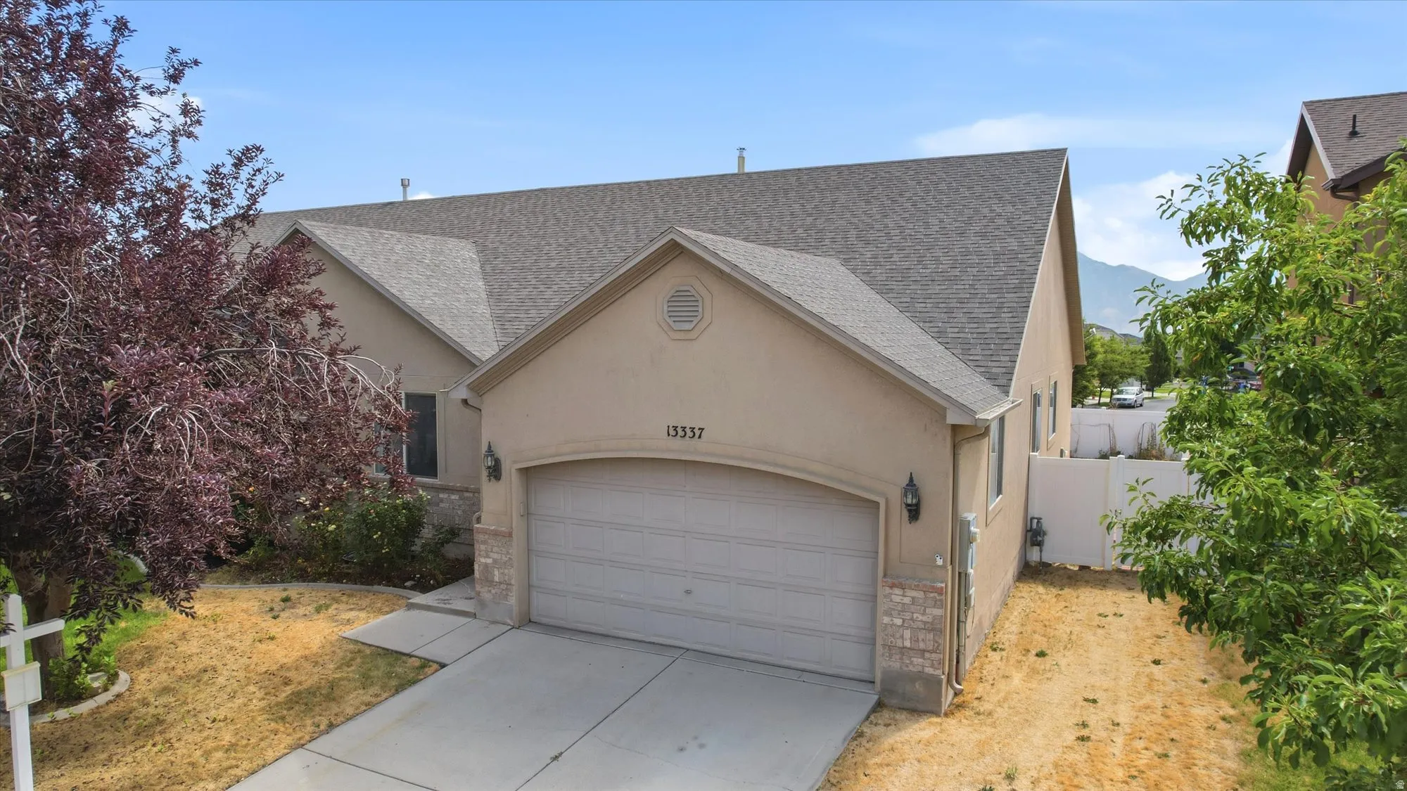Stucco exterior featuring a two-car garage, stone accents, and a shingled roof