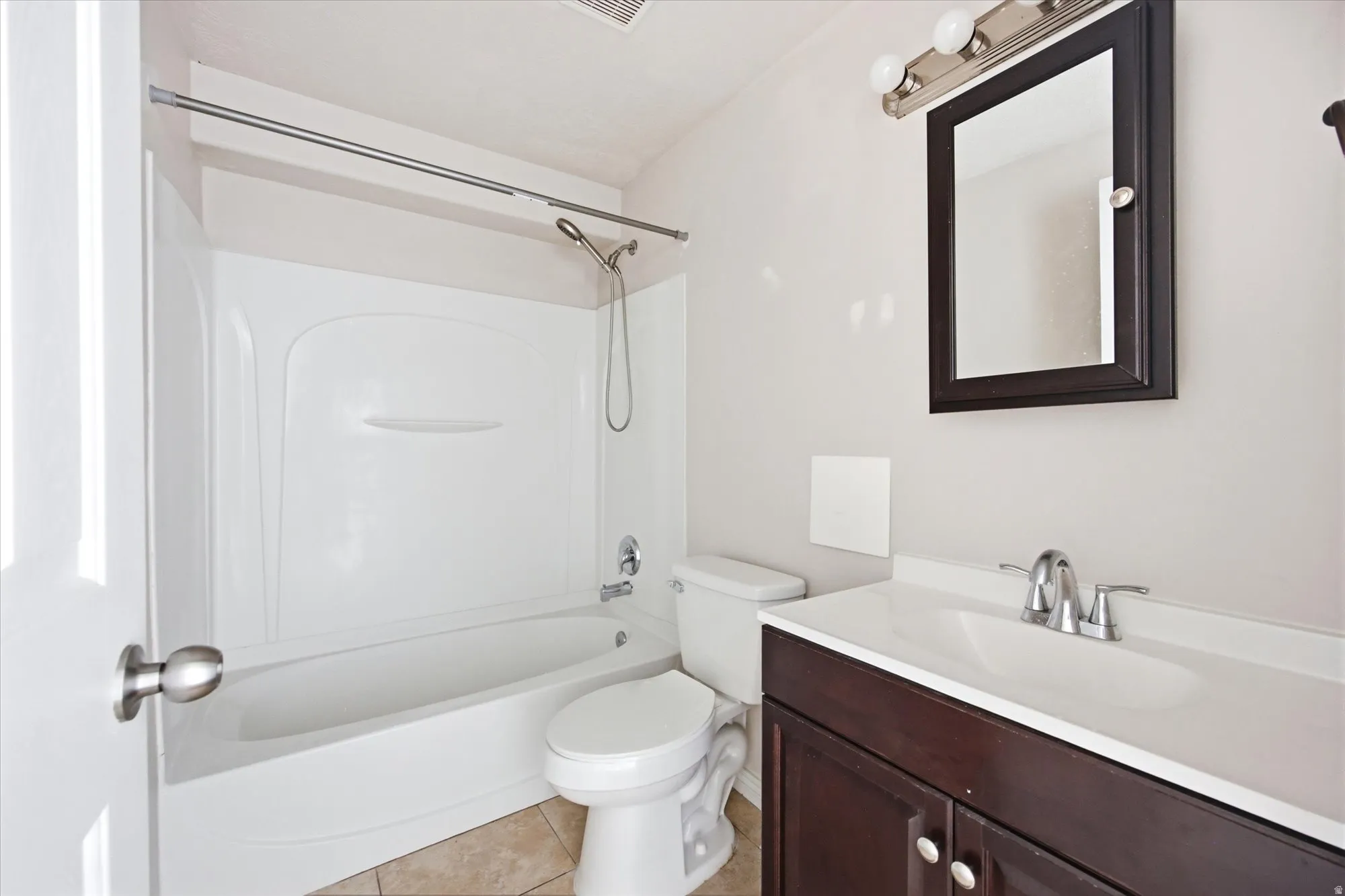 Bathroom featuring a white tub/shower combination, dark wood-finish vanity with an integrated sink, framed wall mirror, and chrome fixtures