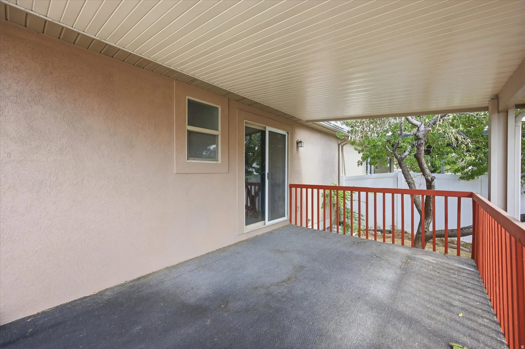 Covered patio featuring a sliding glass door, an adjacent window, and a red-painted wood-spindle railing