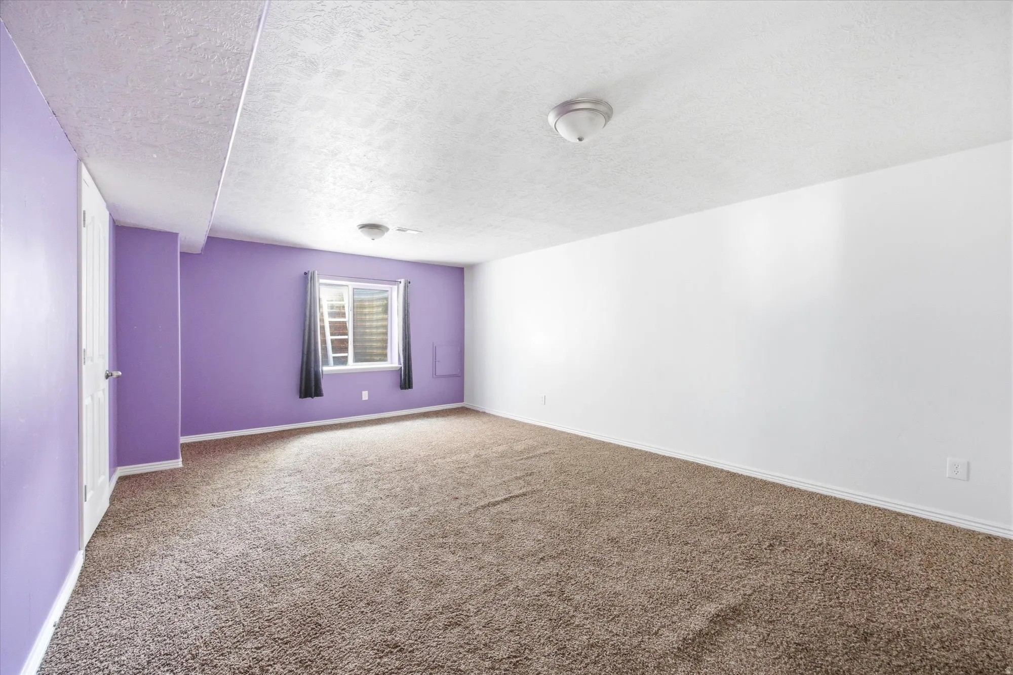 Spacious room featuring neutral carpeting and a window with gray drapes