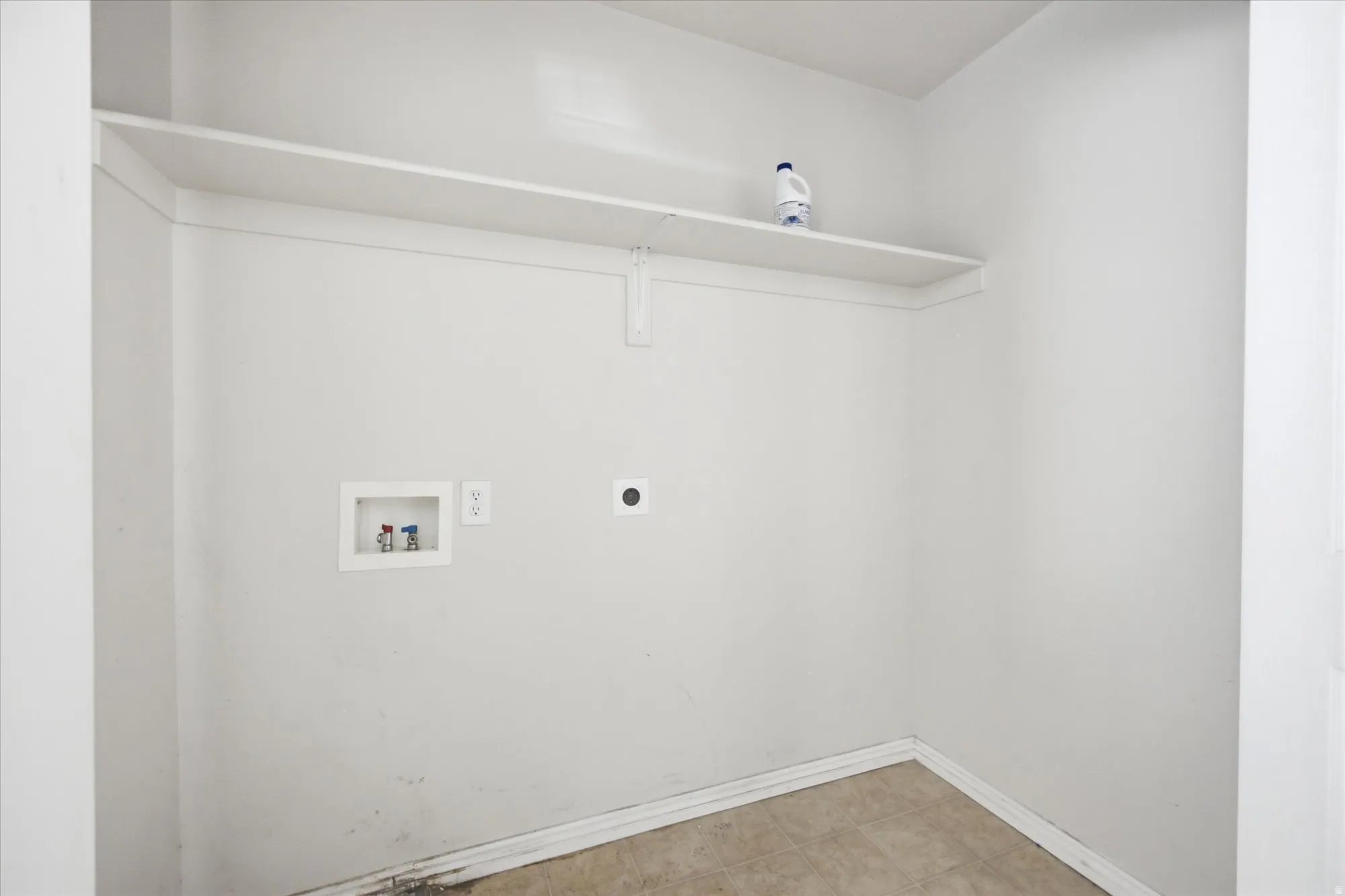 Dedicated utility space featuring a wall-mounted shelf, washer/dryer hookups, and light-toned flooring