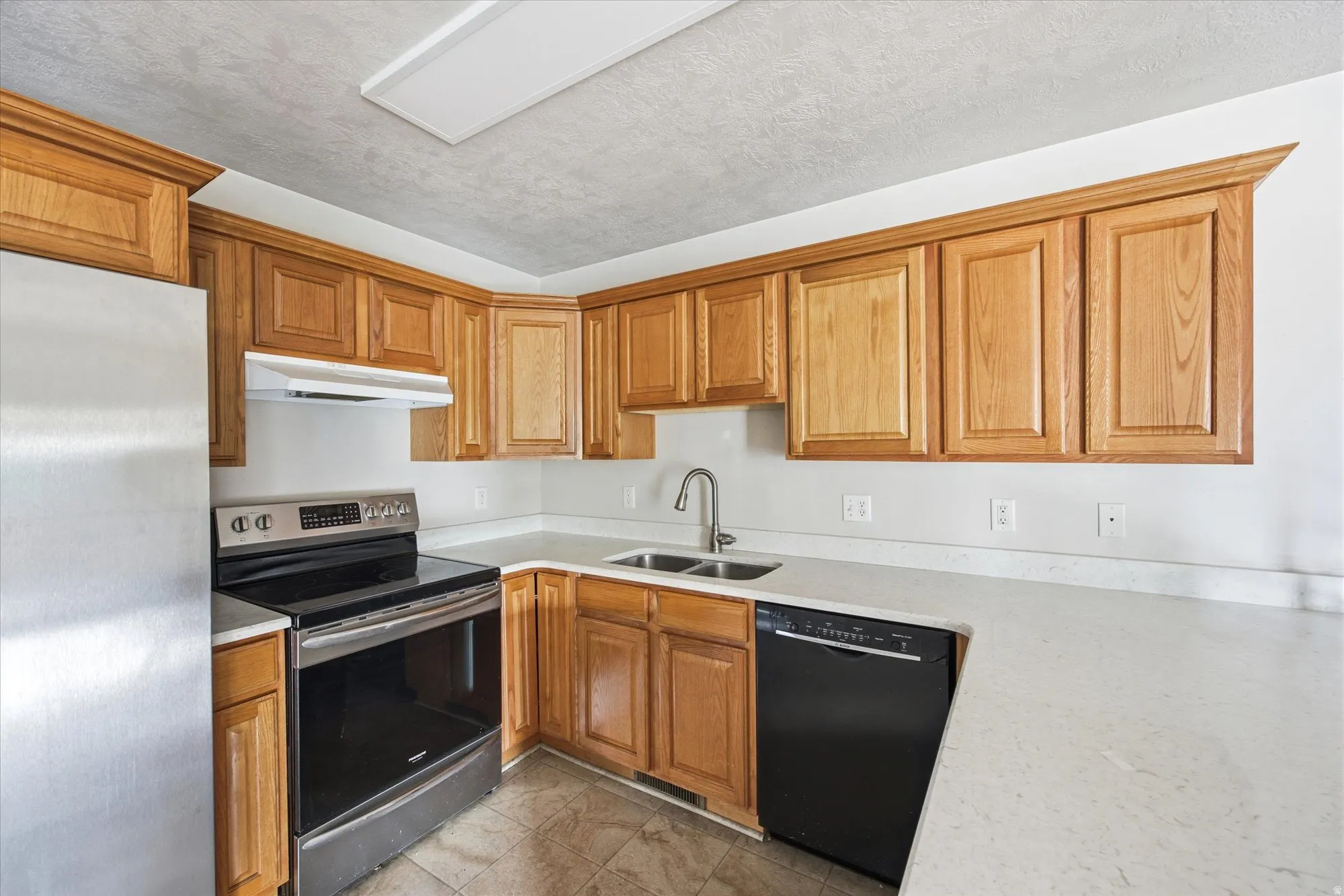 Kitchen featuring light wood cabinetry, light countertops, stainless steel refrigerator, stainless steel range, and a black dishwasher