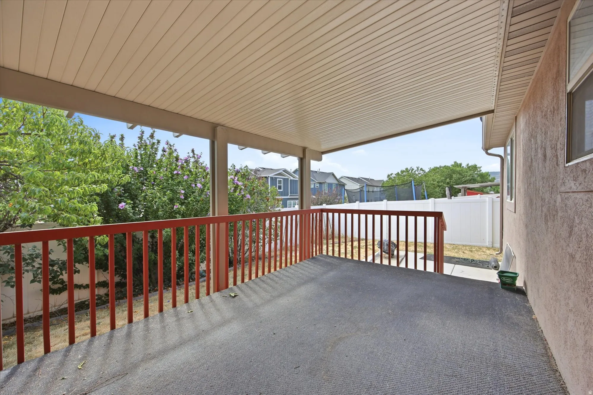 Covered patio featuring a slatted ceiling, red wooden railing, and a textured floor