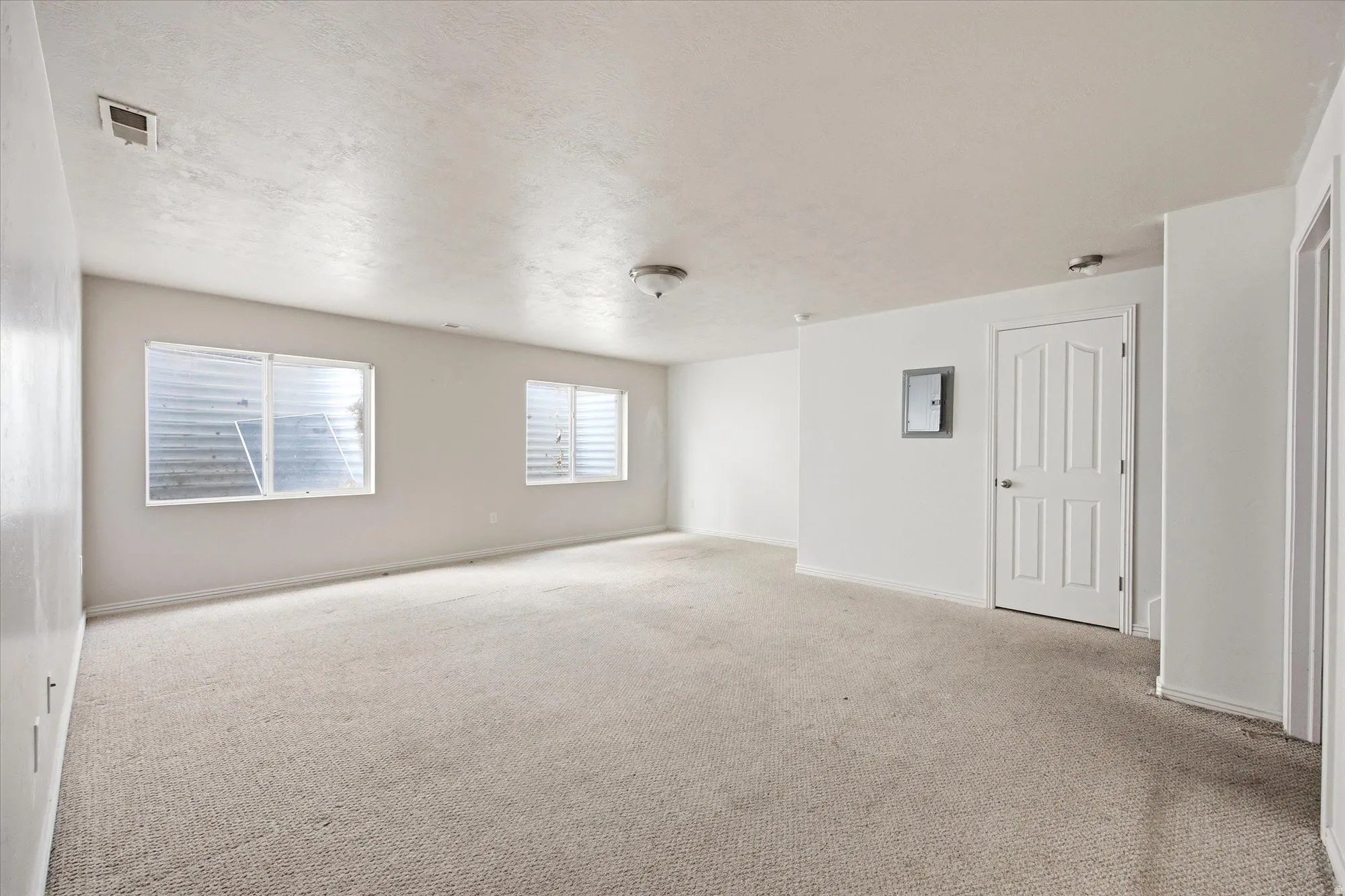 Spacious carpeted room featuring two horizontal windows with white frames and security bars