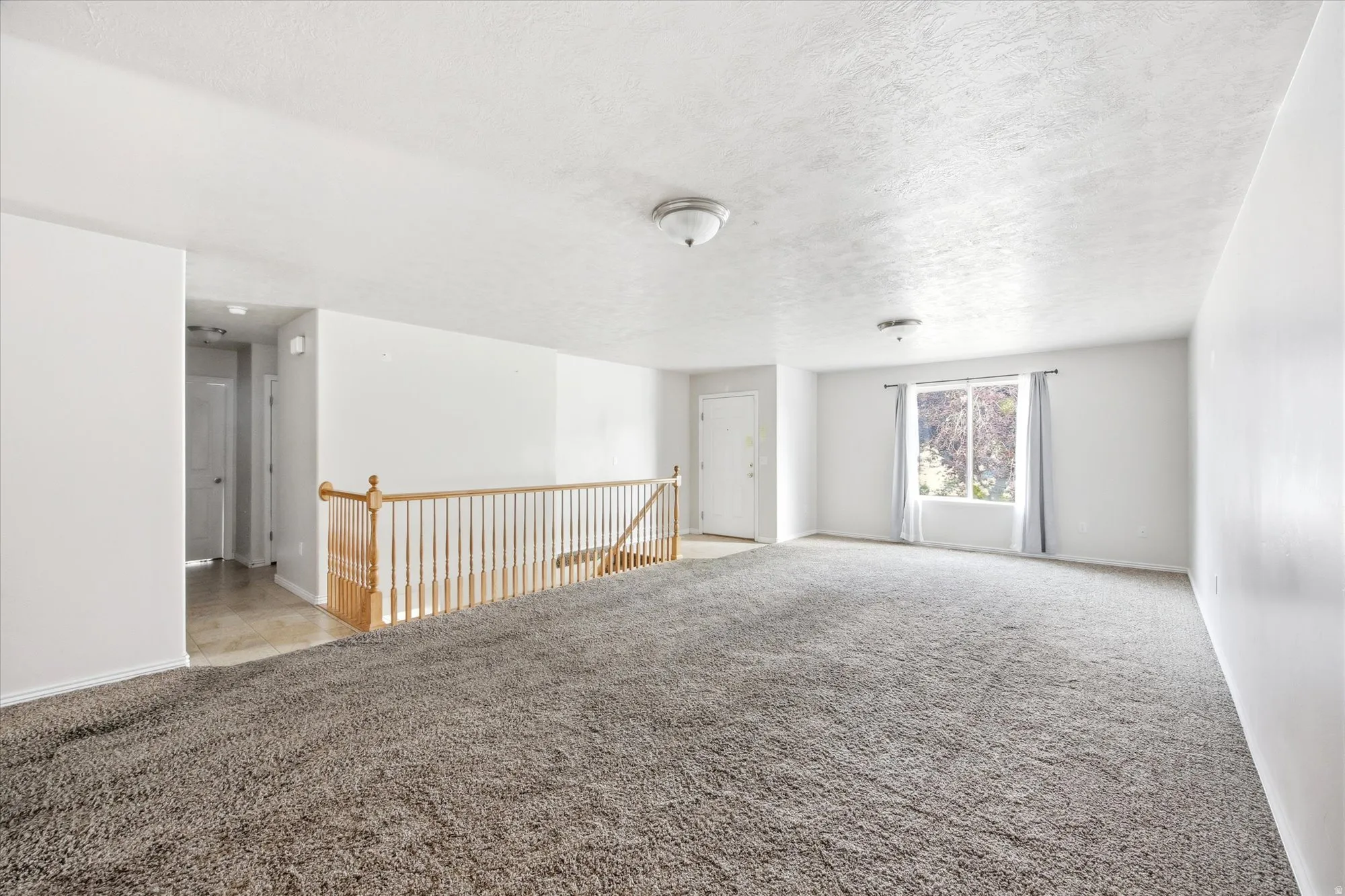 Spacious living area featuring neutral carpeting, white walls, and abundant natural light from the large window