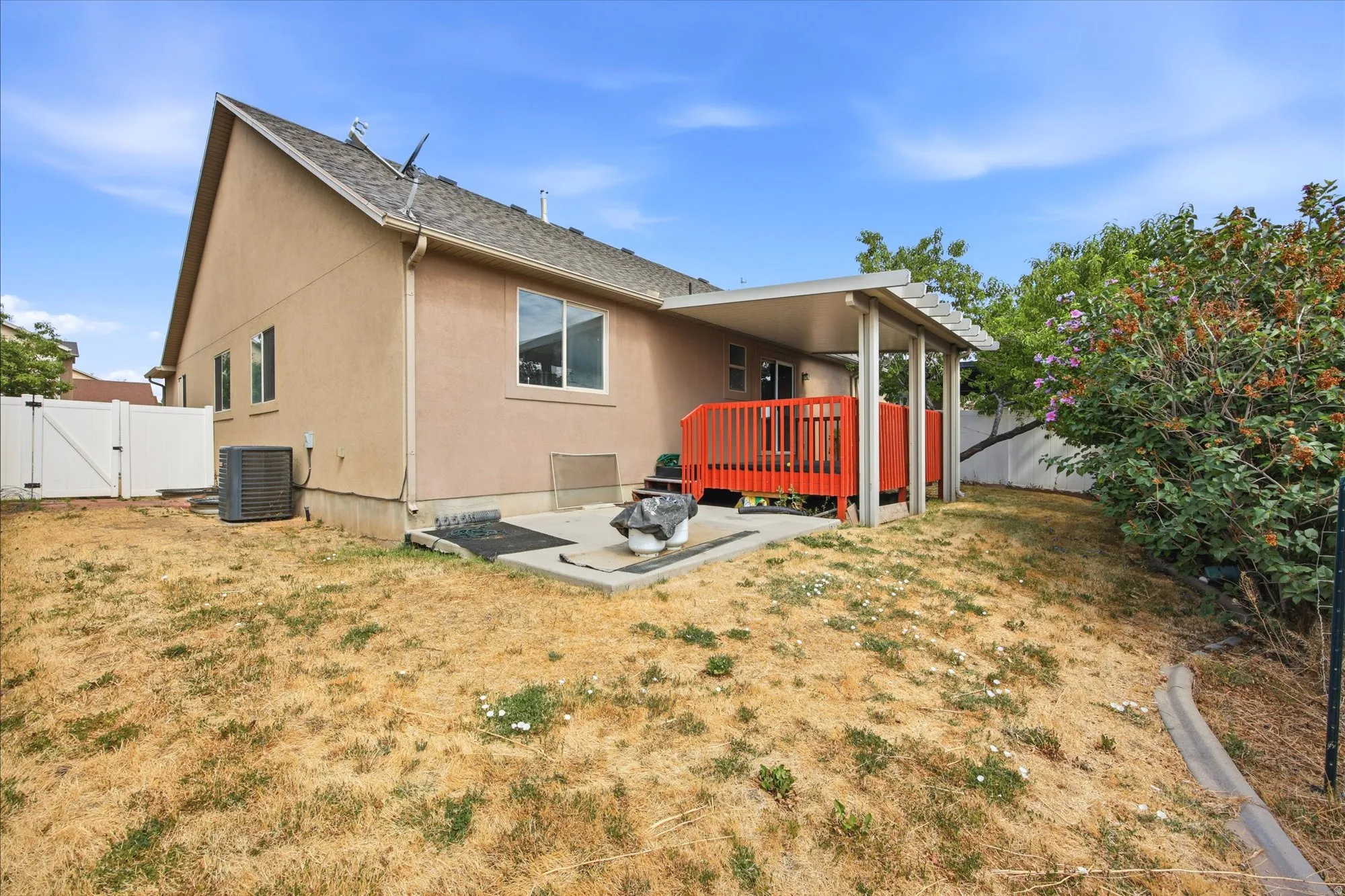 Rear exterior featuring a covered deck with red railing, an additional concrete patio, and stucco siding