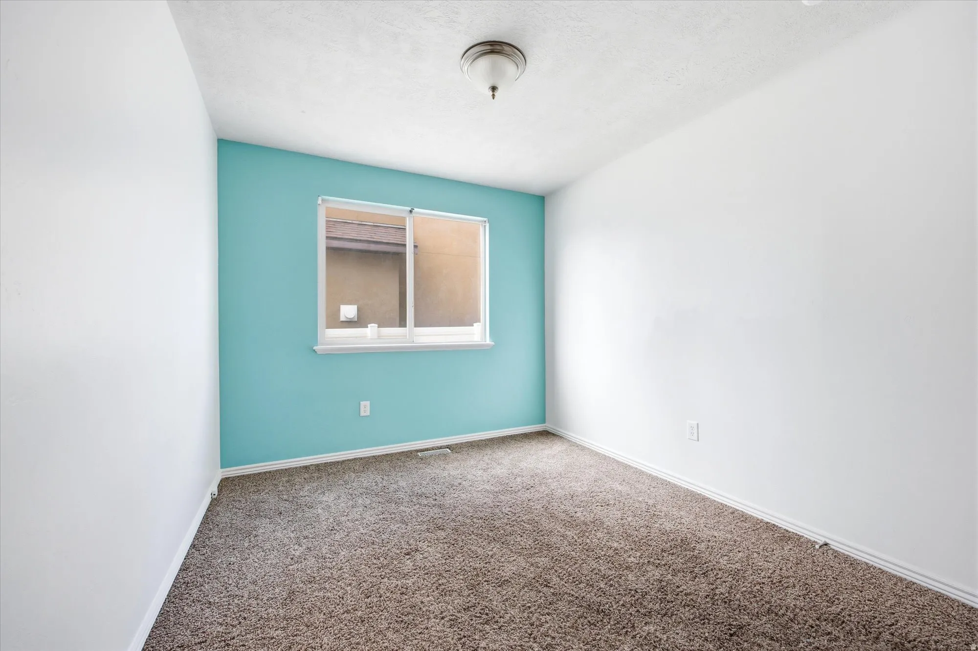Bright interior space featuring a window with white trim, a turquoise accent wall, white baseboards, and brown carpet