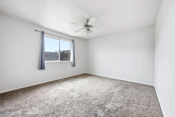 Bright room featuring a large window, neutral carpeting, white walls, and a ceiling fan with integrated lighting