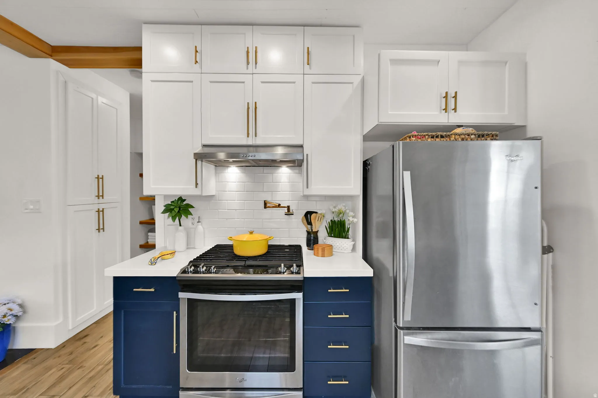 Modern kitchen featuring two-tone cabinetry, stainless steel appliances, a white subway tile backsplash, and gold pot filler over range
