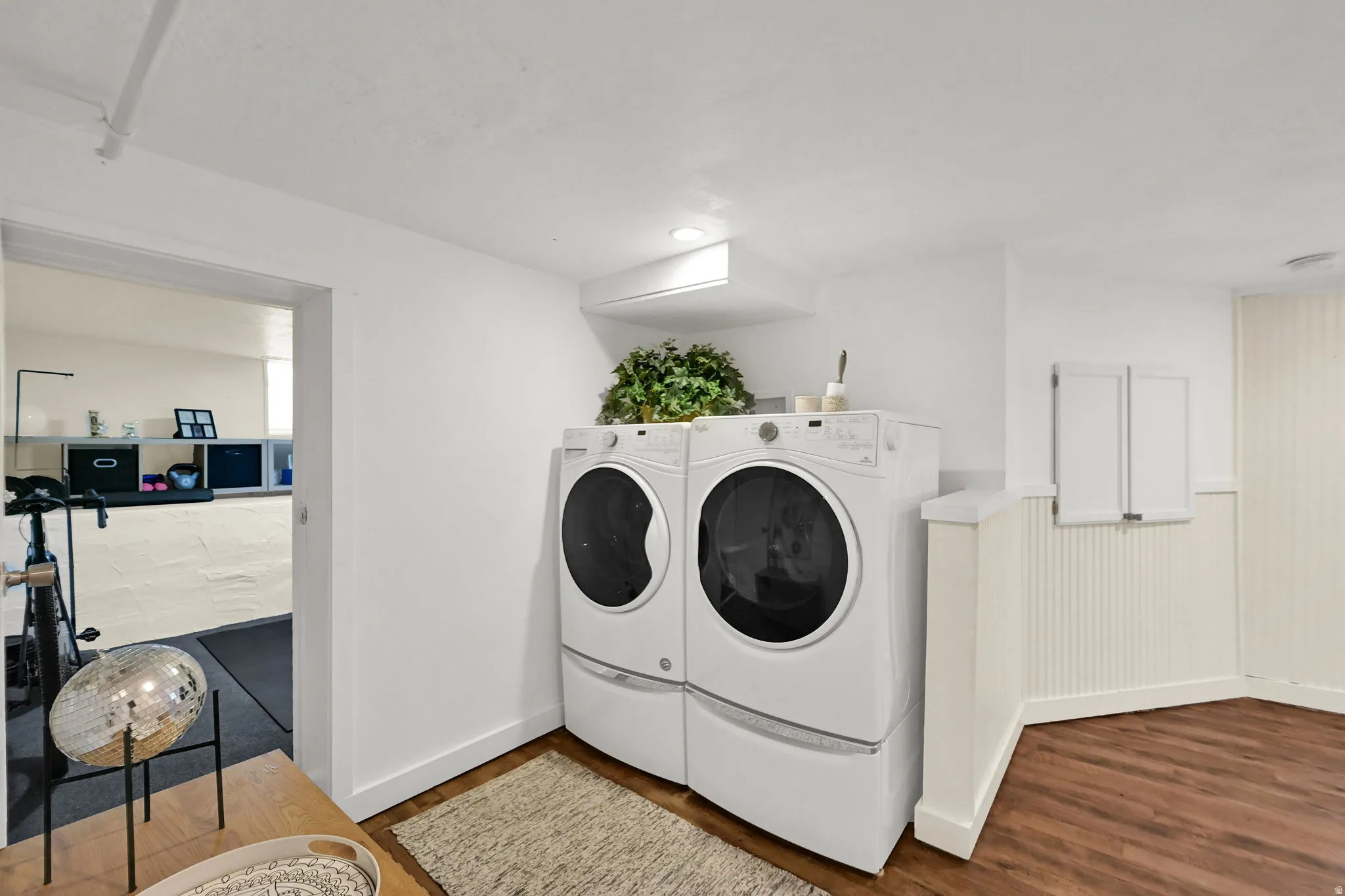 Dedicated laundry area featuring a white stacked washer and dryer set, wood-finish flooring, and wainscoting detail