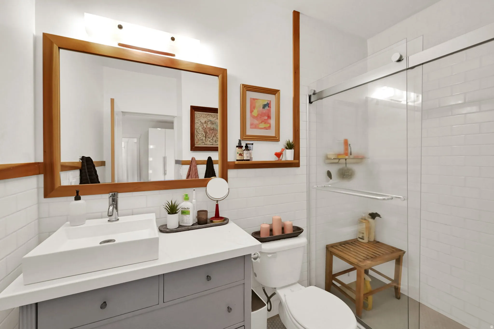Primary ensuite bathroom featuring a white subway tile surround, a rectangular vessel sink, a gray vanity with drawer storage, a large wood-framed mirror, and a glass-enclosed shower with a sliding door