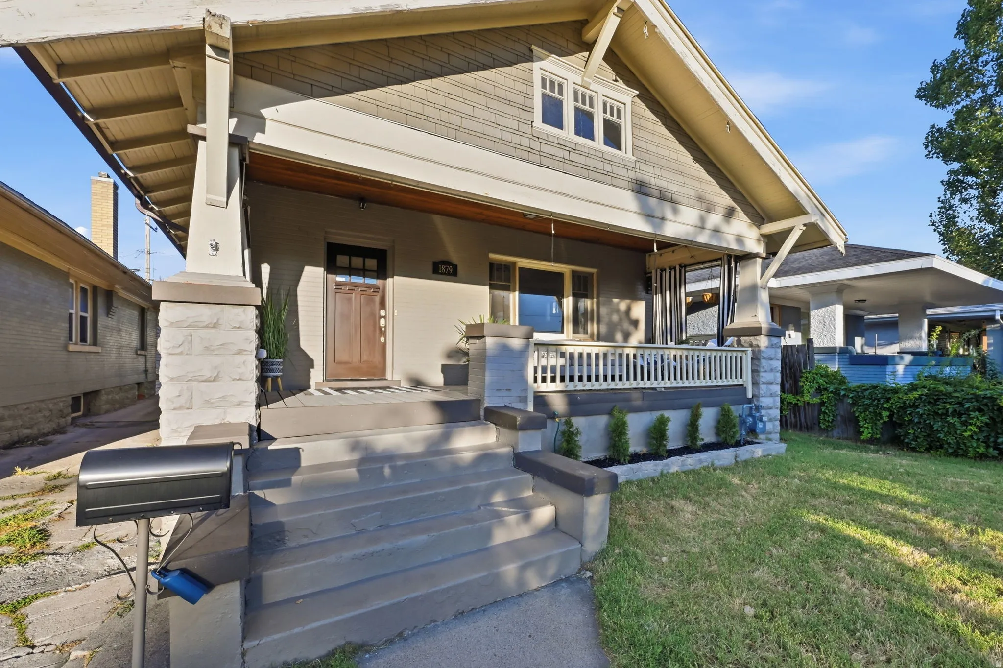 Craftsman-style facade with a covered front porch featuring a wood entry door with glass pane, stone-wrapped columns, and a balustrade railing