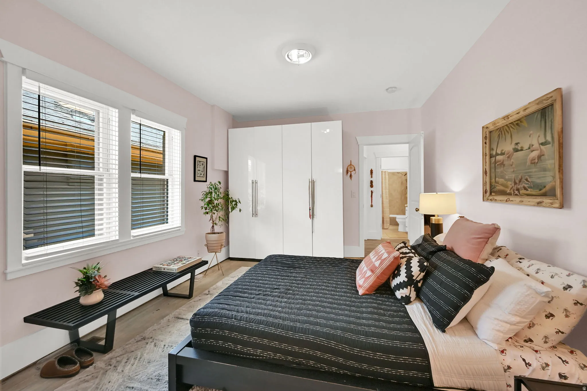 Bedroom featuring wood-finish flooring, dual windows with white trim, and a built-in glossy white wardrobe