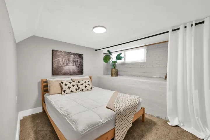 Bedroom featuring light gray walls, a window with blinds, and white painted brickwork