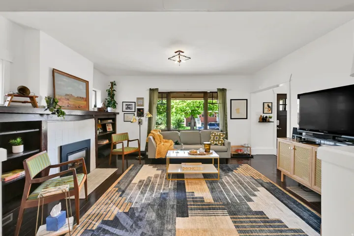 Spacious living area featuring dark wood-finish flooring, a central fireplace with built-in shelving, white tiled surround, and large front-facing windows