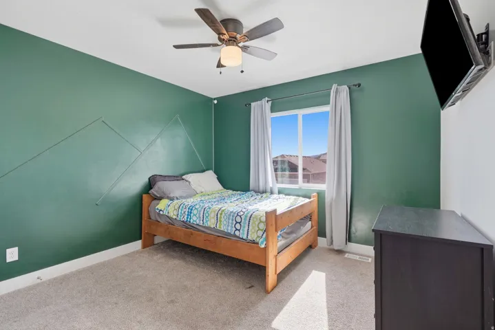 Bedroom featuring a ceiling fan with light fixture, wall-mounted television, and a window with white trim
