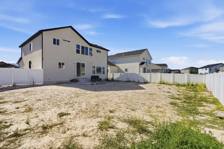Expansive rear yard featuring a concrete patio, white vinyl fencing, and multiple windows across the back facade