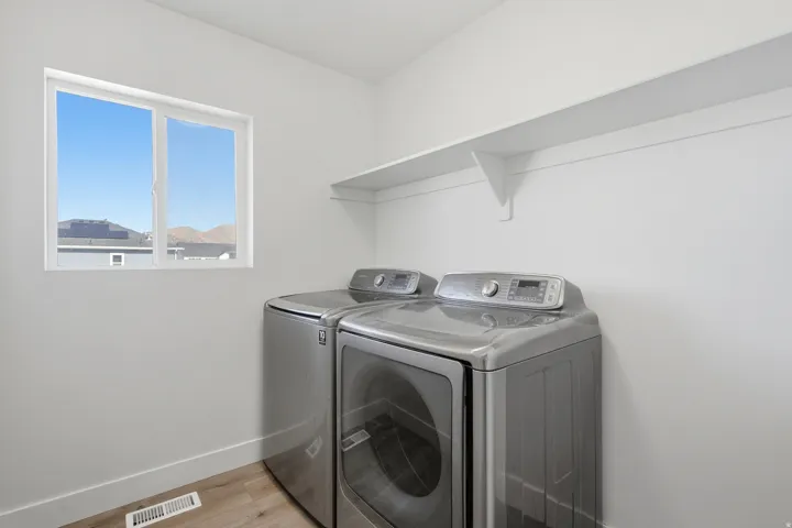 Laundry area featuring light wood-finish flooring, white walls, and a white window with a clear sky backdrop