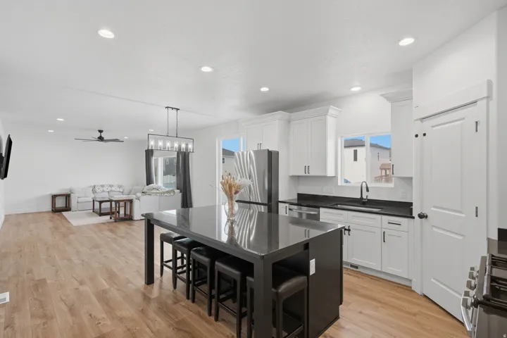 Open-concept living space featuring a kitchen island with seating, wood-finish flooring, recessed lighting, white cabinetry, and stainless steel appliances