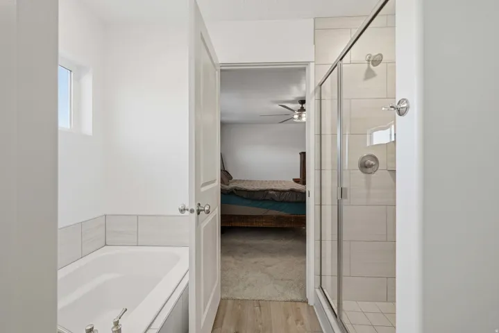 Contemporary bathroom featuring a glass-enclosed shower with tile surround, a built-in tub with tile trim, and light wood-finish flooring