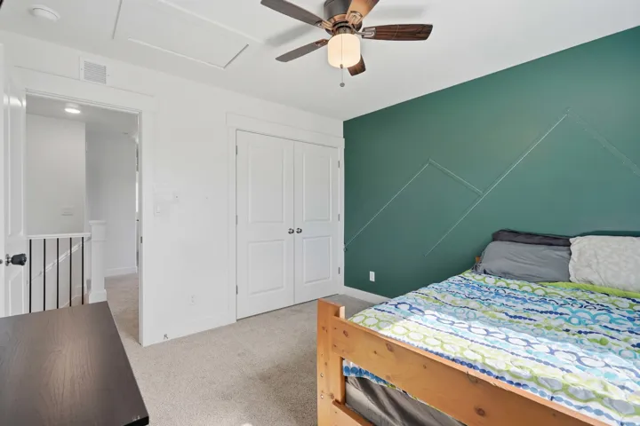 Carpeted room featuring a ceiling fan with light fixture, white trim, and a patterned accent wall
