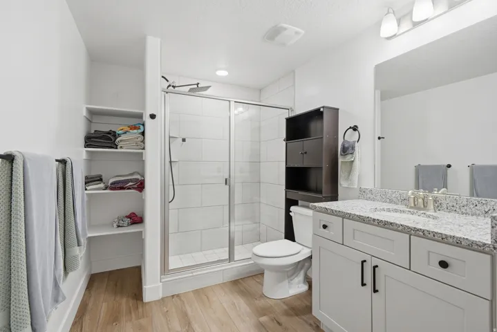 Modern bathroom featuring a glass-enclosed shower with tile surround, a single vanity with granite countertop, and wood-finish flooring