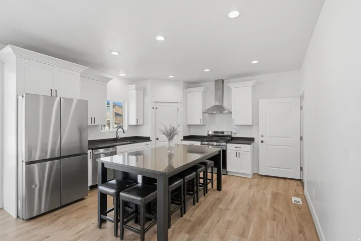Modern kitchen featuring a large central island, light wood-finish flooring, white cabinetry, dark countertops, and stainless steel appliances
