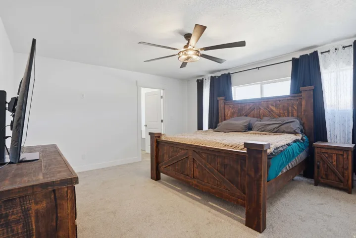 Carpeted room featuring a ceiling fan with integrated lighting, white walls, and a window with dark and sheer curtains