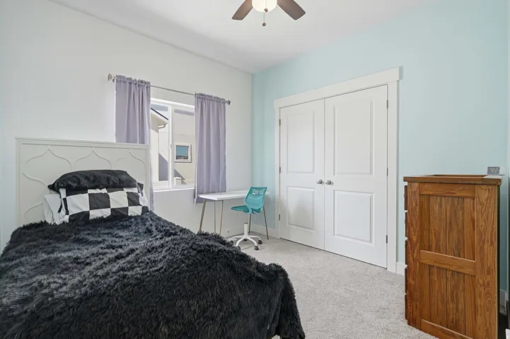 Bedroom featuring a white framed window with curtains, light blue and white walls, a ceiling fan, and double-door closet with white trim