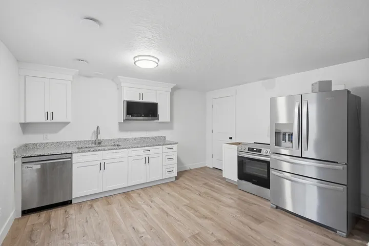 Contemporary kitchen featuring white shaker cabinetry, granite-finish countertops, and stainless steel appliances including a refrigerator, range, microwave, and dishwasher