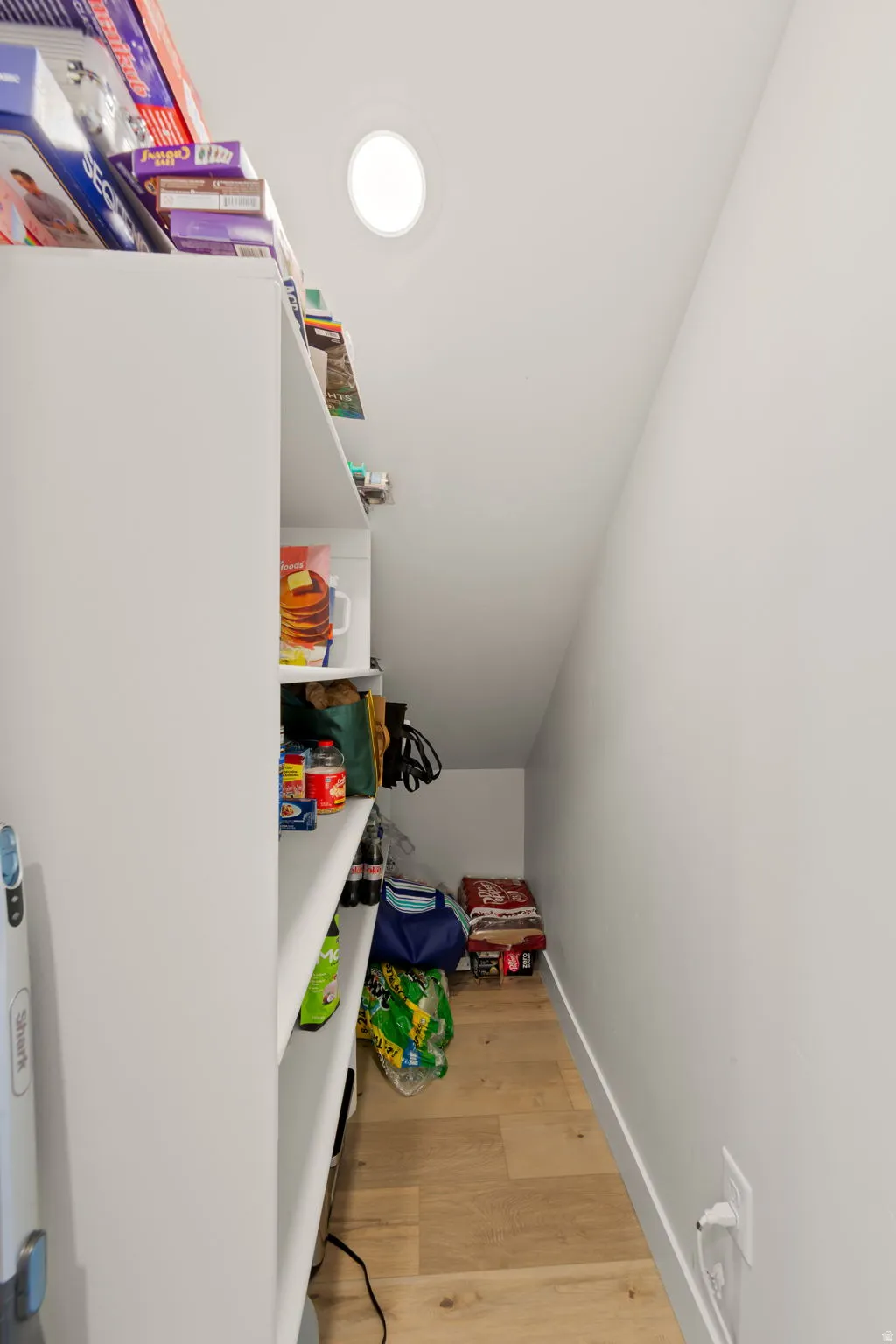 Pantry featuring built-in shelving, wood-finish flooring, and sloped ceiling
