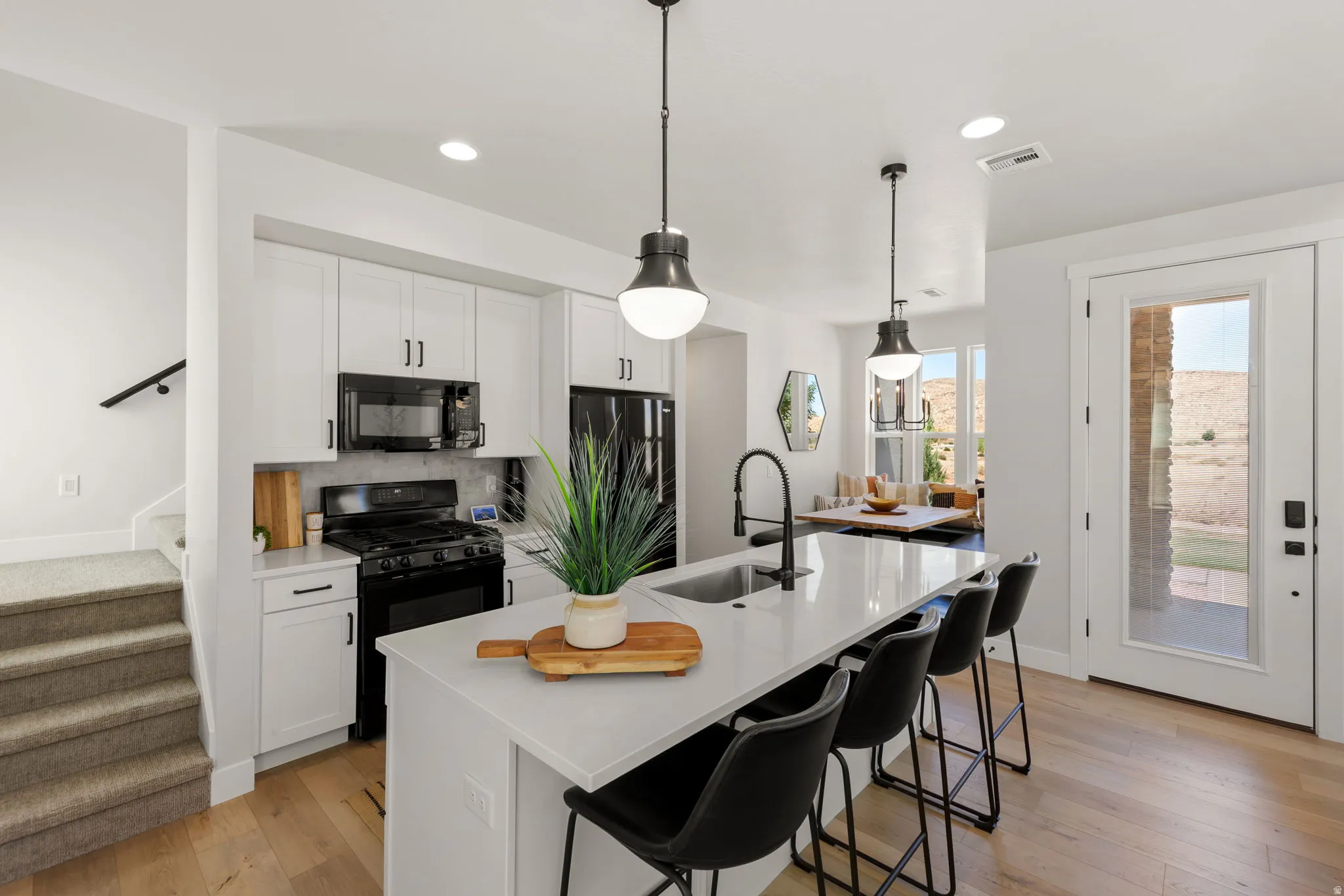 Modern kitchen featuring white cabinetry, black appliances, a central island with bar seating, pendant lighting, and wood-finish flooring