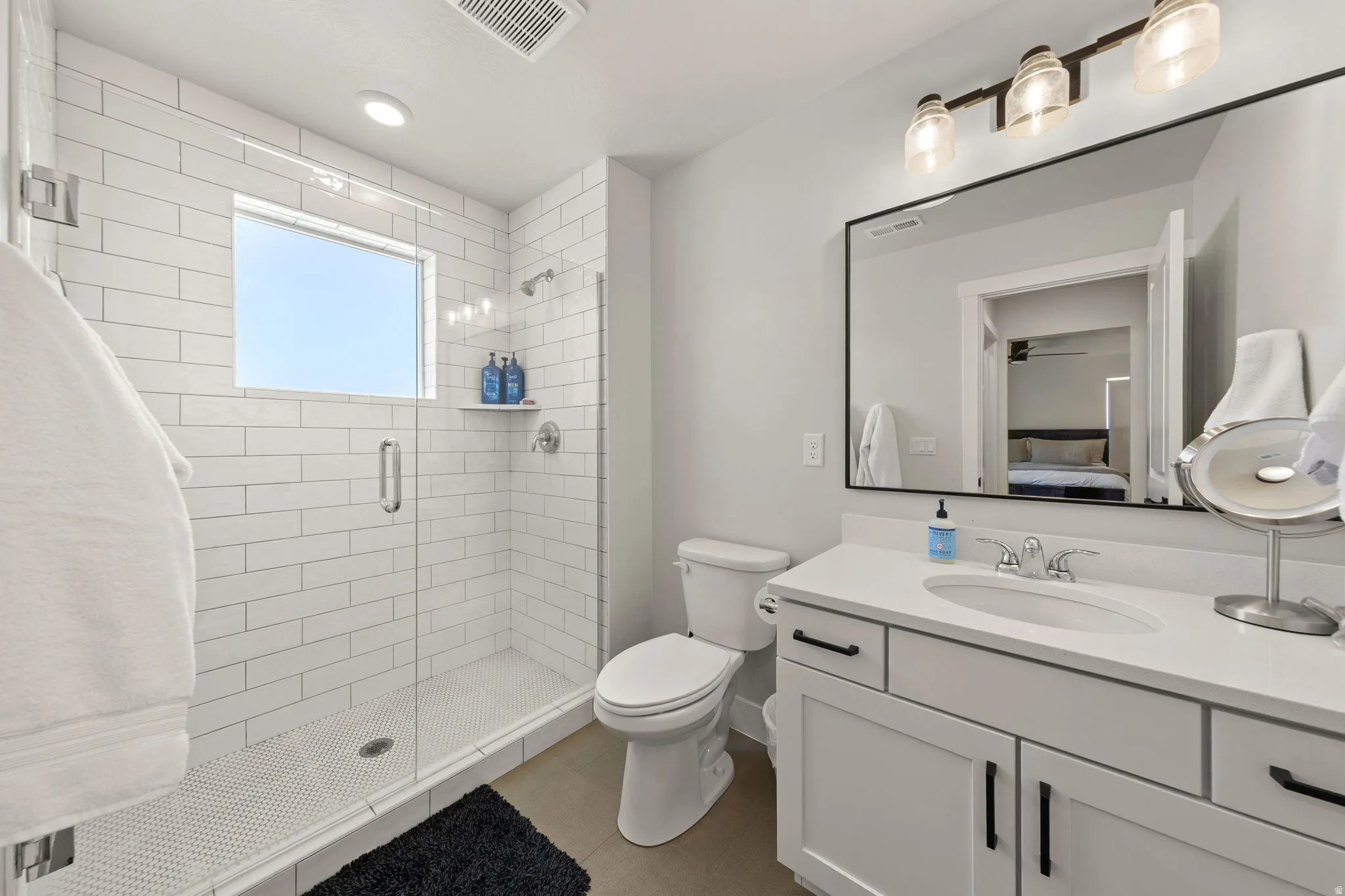 Bathroom featuring a glass-enclosed shower with subway tile surround and a window