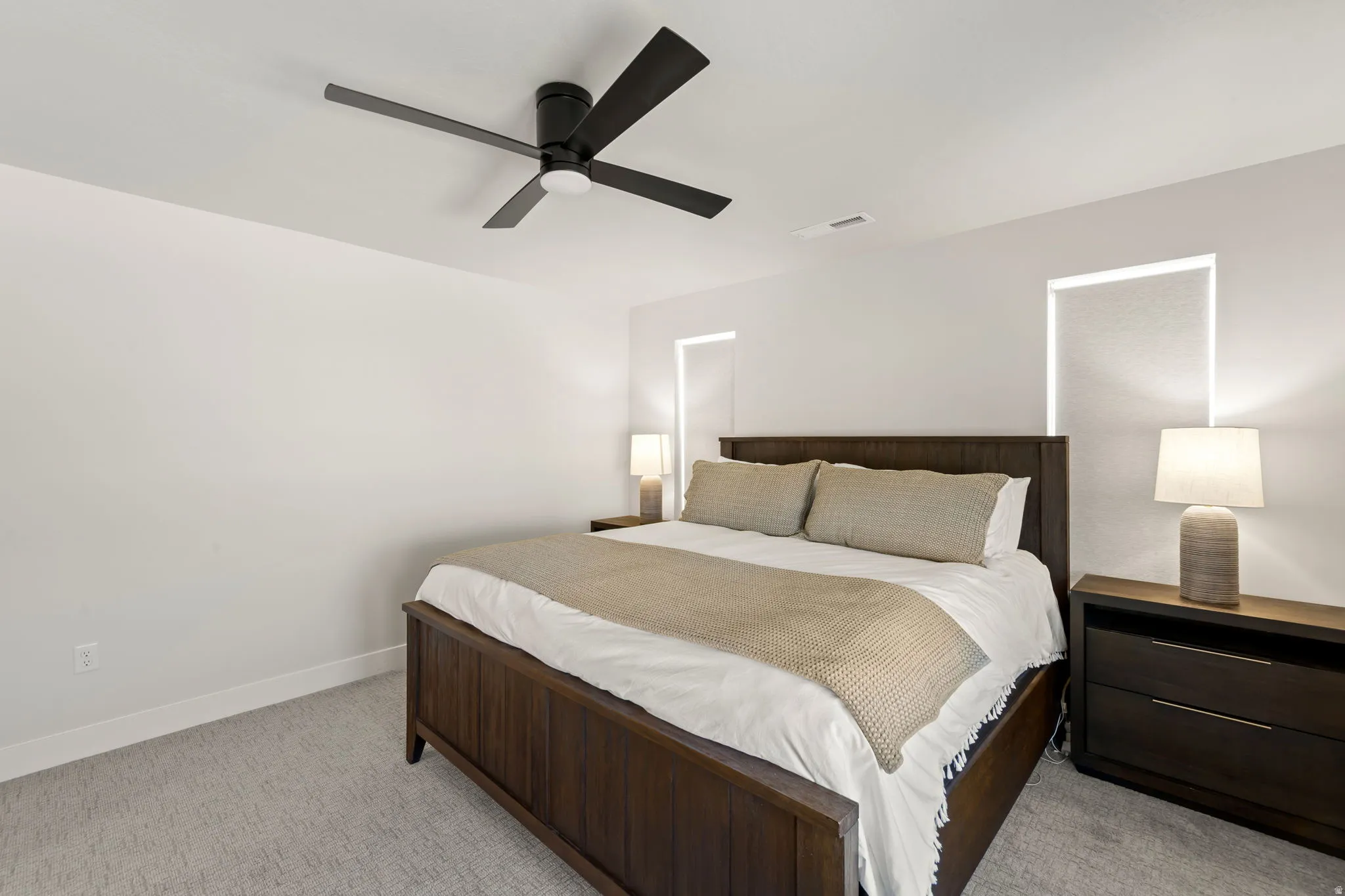Bedroom featuring light gray carpeting, crisp white walls, a black ceiling fan, and recessed window openings