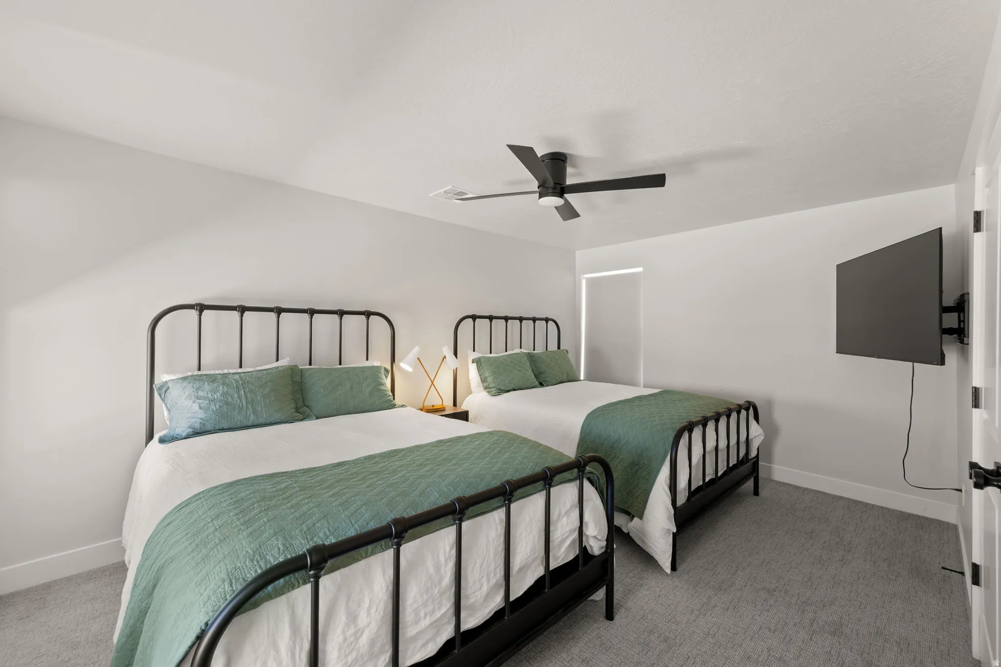 Carpeted bedroom with a matte black ceiling fan, white walls, and a wall-mounted television