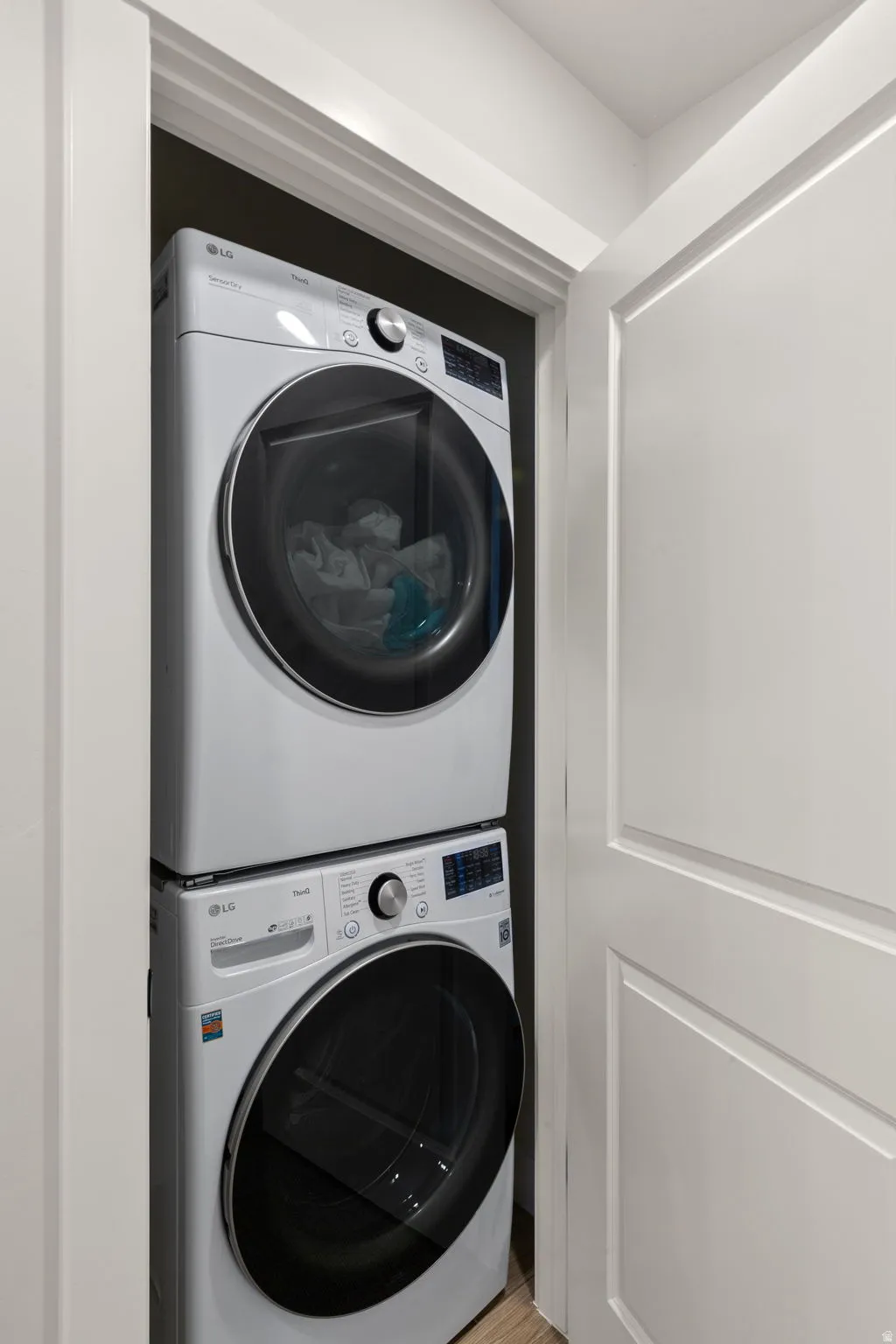 Stackable washer and dryer units in a dedicated closet, featuring white panel doors and light wood-finish flooring